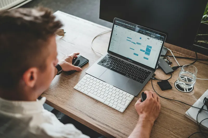Iemand werkt aan een laptop, met een telefoon ernaast